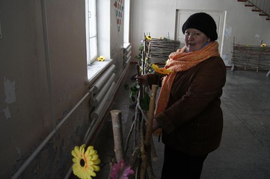 Любовь Юрьевна Лушникова демонстрирует облупившуюся штукатурку стен фойе, «задекорированных» плетнями.